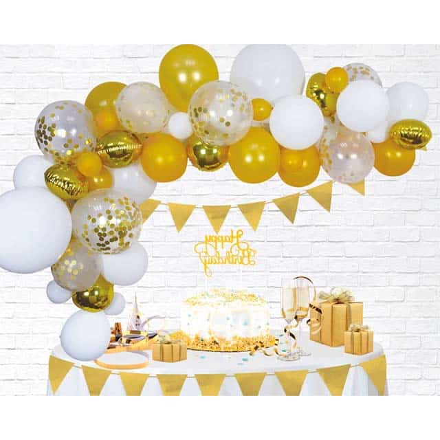 Goud-witte ballonnenboog van 4 meter boven een feesttafel met taart, cadeaus en gouden vlaggetjes