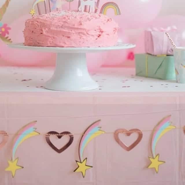 Van dichtbij hangt de Feestslinger Hearts en Shooting stars langs de voorkant van een roze tafel, onder een verjaardagstaart