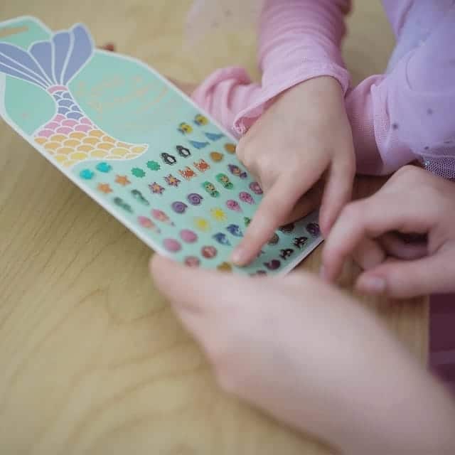 Een kind kiest kleurrijke oor stickers uit een vel met zeemeermin oorstickers en andere zeedierfiguren.