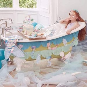 Meri Meri zeemeermin slingers versieren een bad met pastelkleuren, terwijl een meisje in een blauwe zeemeerminstaart zit