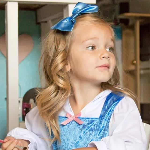 Meisje draagt de belle jurk met blauw rozenpatroon, witte mouwen, roze borststrik en grote blauwe haarstrik
