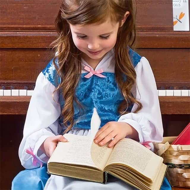 Meisje leest in een boek terwijl ze een blauwe Belle jurk draagt met wit schort en lange mouwen.