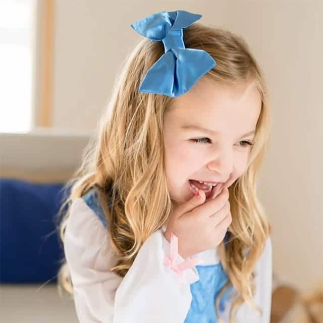 Meisje draagt een blauwe Belle jurk met witte mouwen en een grote blauwe haarstrik.