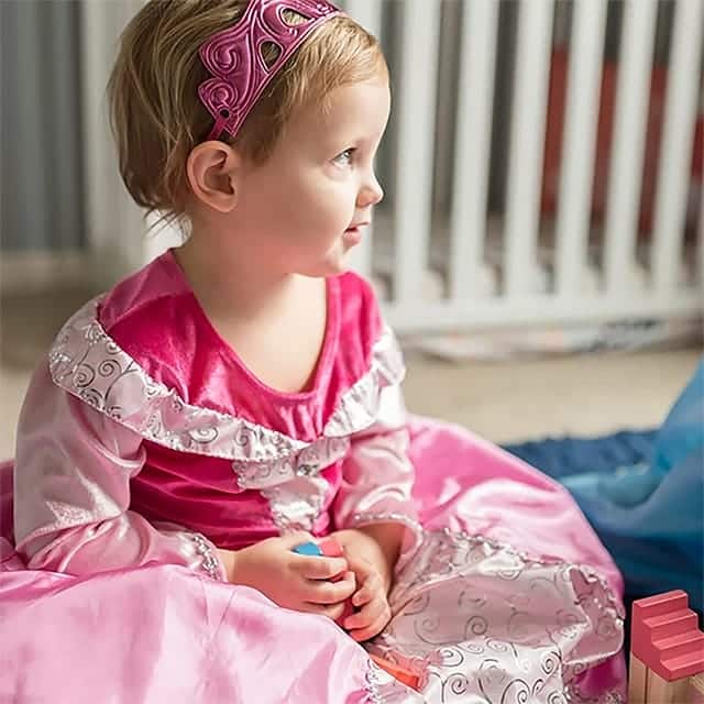 Meisje draagt de roze Doornroosje classic jurk met zilveren versiering en een roze tiara, zittend op de vloer.