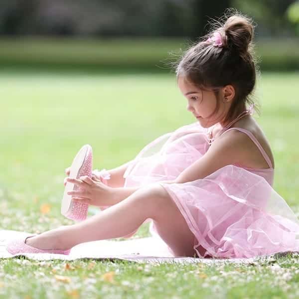 Meisje in roze tutu draagt en toont roze glitter schoenen van Rose & Romeo op het gras
