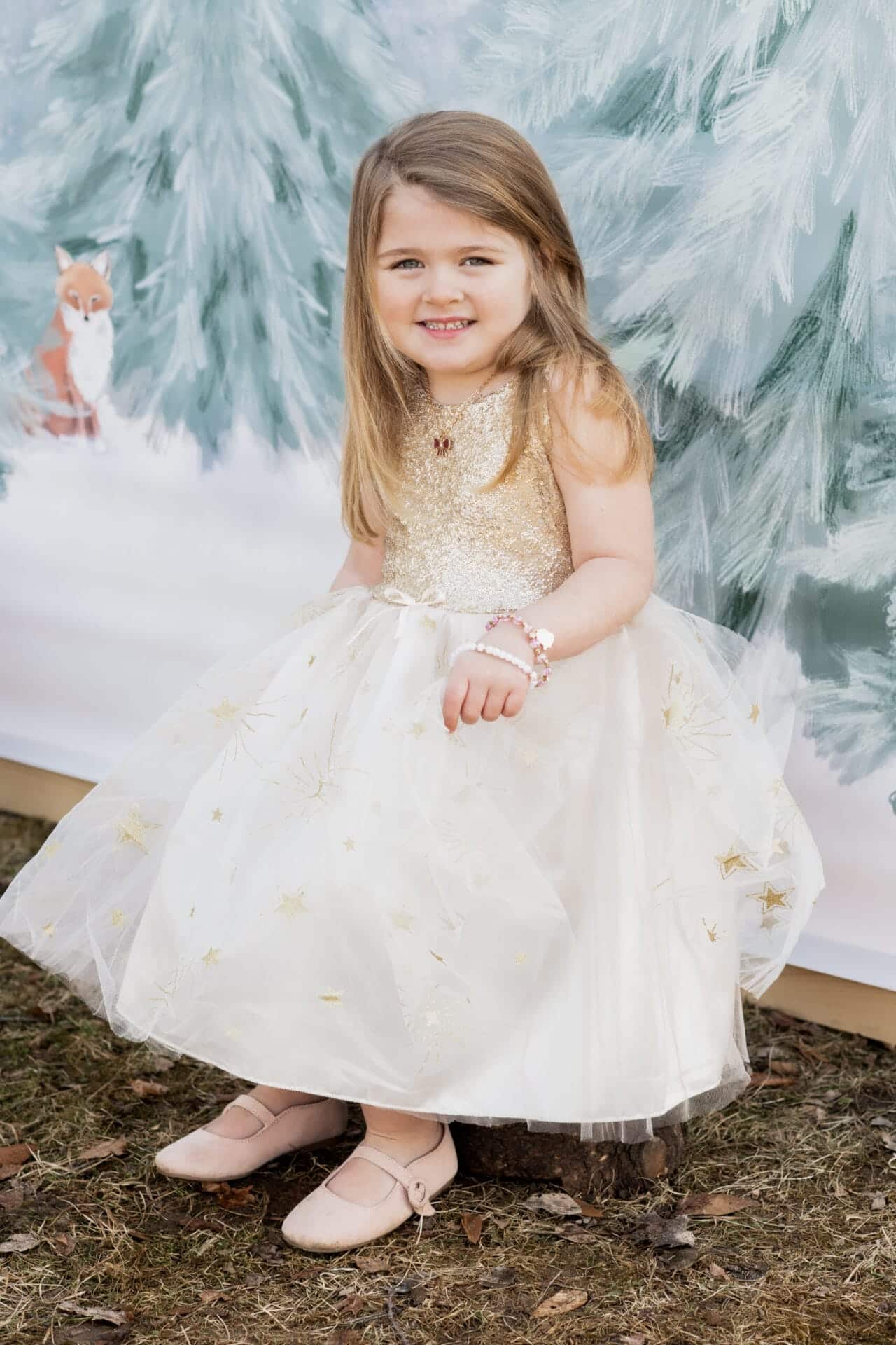 Meisje draagt een witte Great Glam-feestjurk met gouden lijfje en sterren op de rok, tussen besneeuwde bomen.