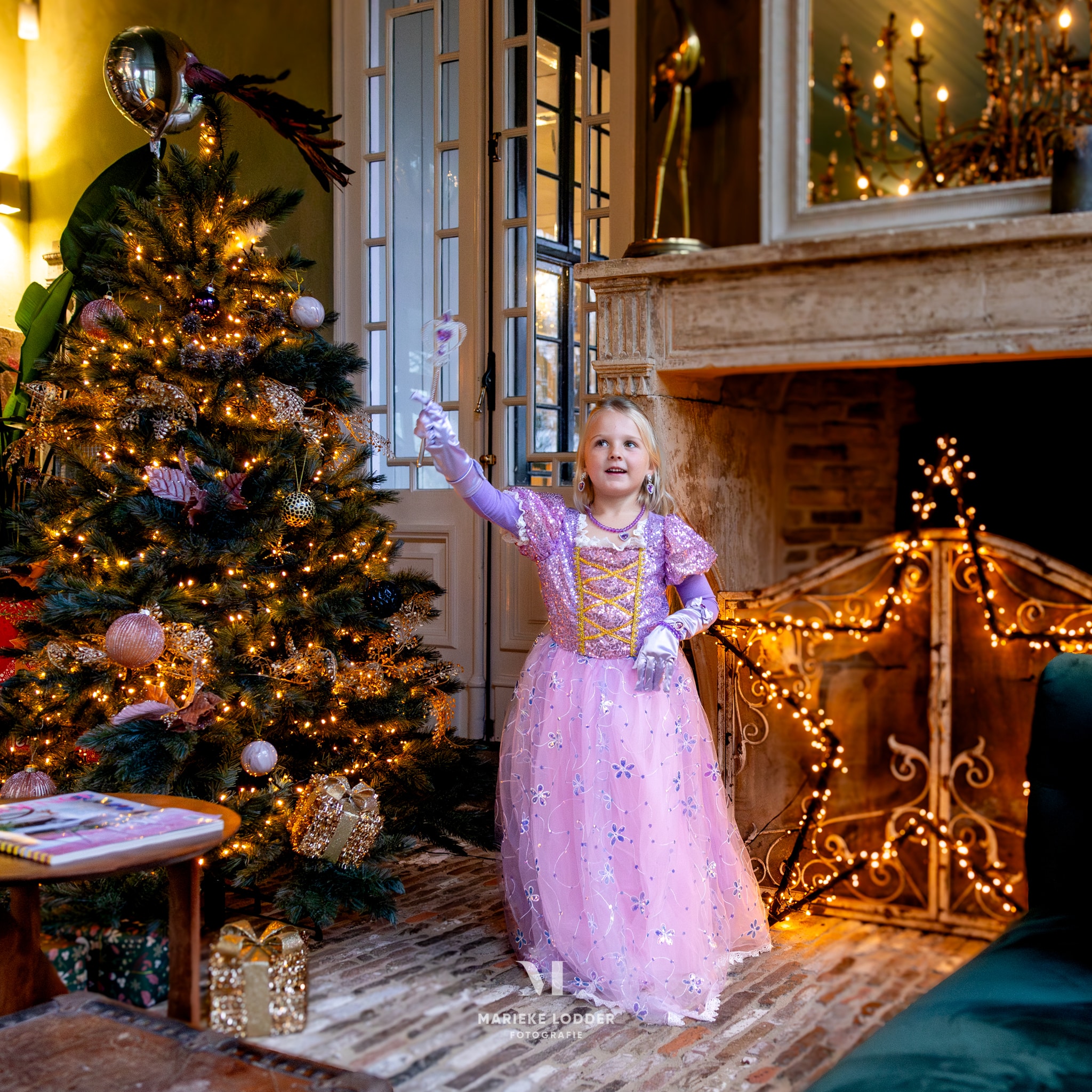 Meisje draagt een roze Rapunzel verkleedjurk met glitterdetails en handschoen naast een versierde kerstboom.