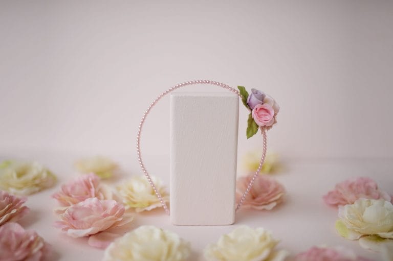 Roze haarband met parels en roze roosjes van Great Pretenders, hangend rond een witte standaard tussen bloemen