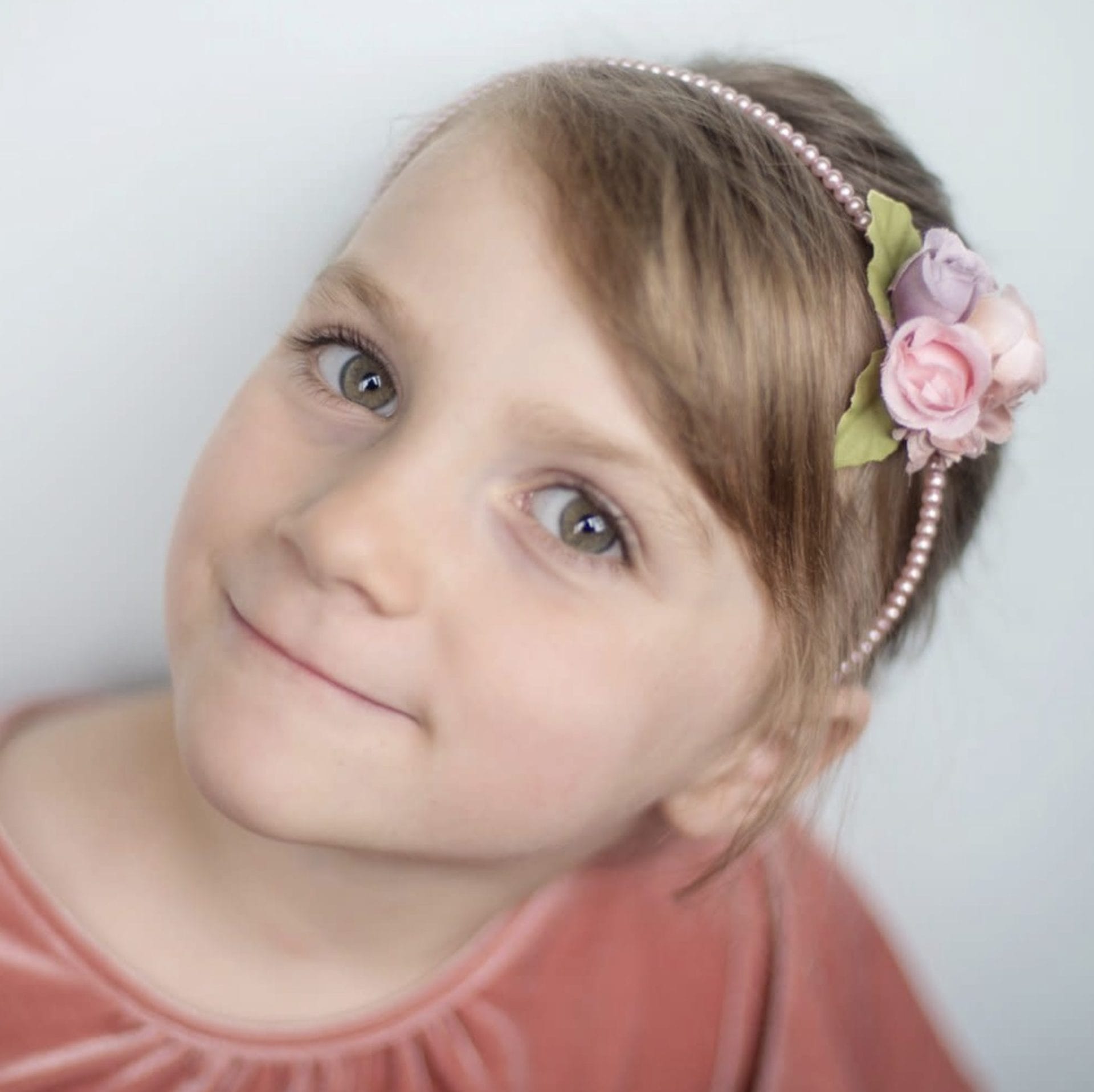 Meisje draagt een roze haarband parels met roze roosjes, zichtbaar rond haar hoofd.