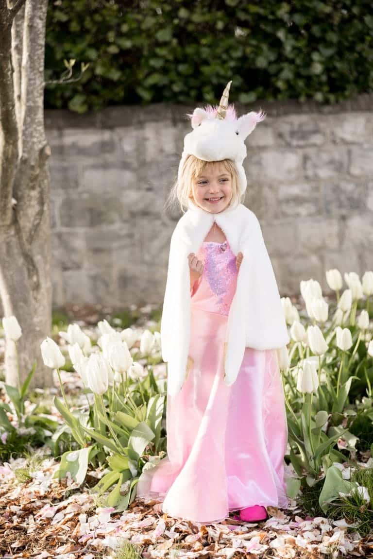 Meisje draagt de witte Eenhoorn knuffelcape met eenhoornkap over een roze jurk tussen witte tulpen