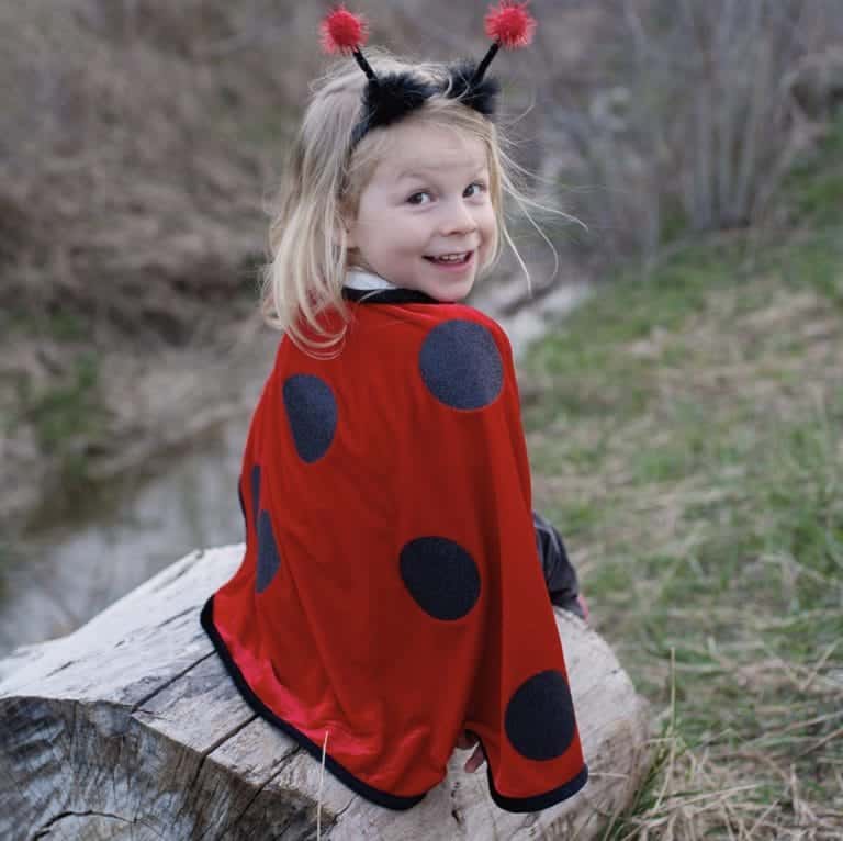 Meisje draagt een rood lieveheersbeestje kostuum met zwarte stippen en een hoofdband met rode pompons