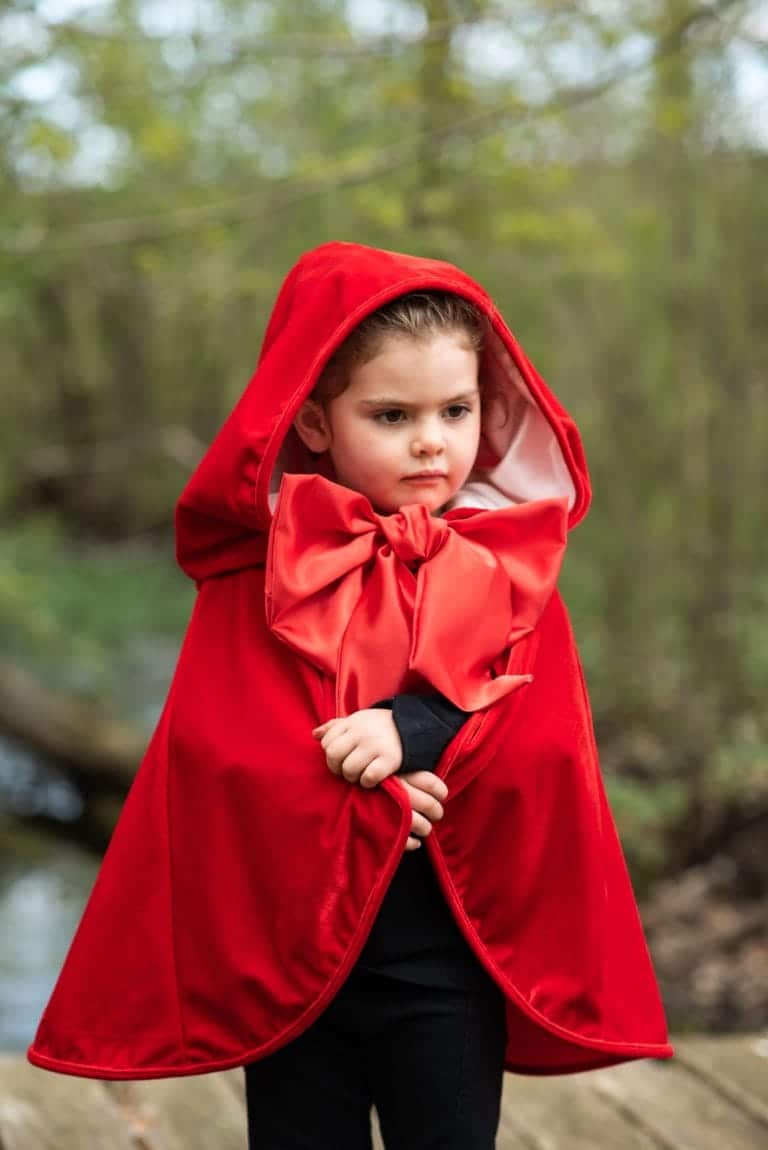 Kind draagt een rode Roodkapje cape met capuchon en grote satijnen strik in het bos