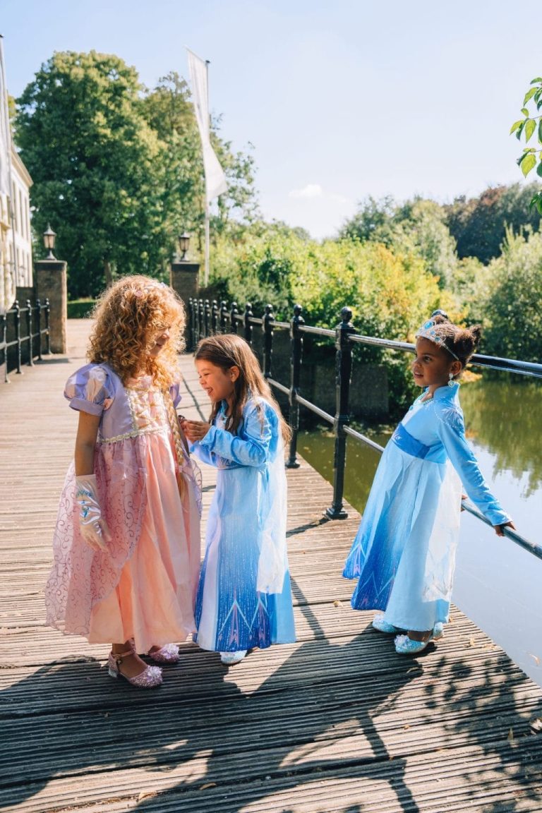 Drie meisjes dragen samen een Elsa en Anna jurk op een houten brug, met blauwe en roze prinsessenjurken