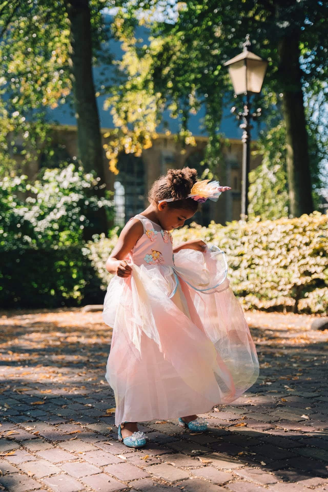 Meisje draagt een roze unicorn verkleedjurk met tule rok, haarband en glinsterende schoenen in het park.