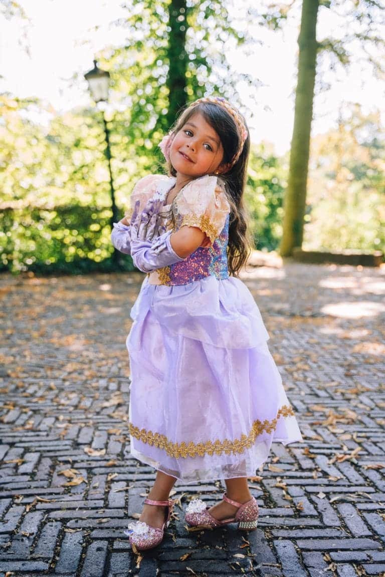 Een kind draagt een paarse rapunzel jurk met gouden details, roze mouwen en lange paarse handschoenen buiten.
