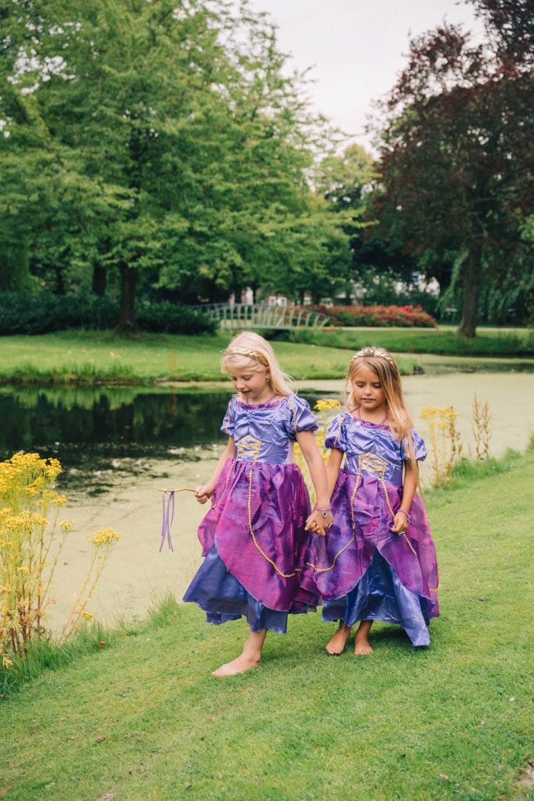 Twee meisjes dragen paarse rapunzel jurken met gouden details aan de rand van een vijver