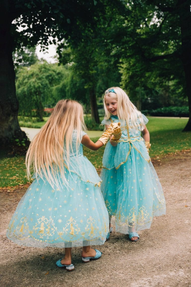 Twee meisjes dragen turquoise Jasmine jurken met gouden versieringen en bijpassende handschoenen in een park