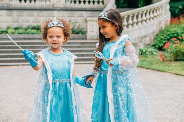 Twee meisjes dragen een blauwe Elsa prinsessenjurk met tiara, handschoenen en doorschijnende cape buiten bij een paleis.