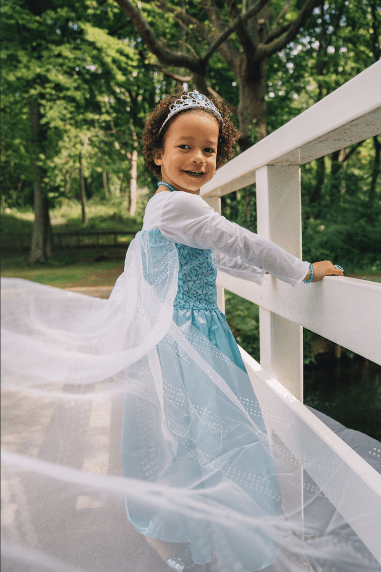 Meisje draagt een blauwe Elsa-prinsessenjurk met witte mouwen en tiara op een witte brug in het bos.
