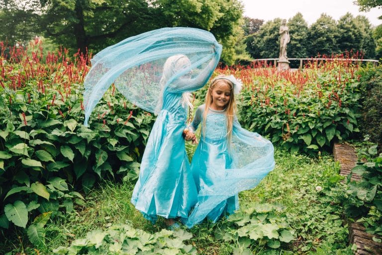 Twee meisjes dragen een blauwe Elsa jurk met doorschijnende cape in een bloeiende tuin
