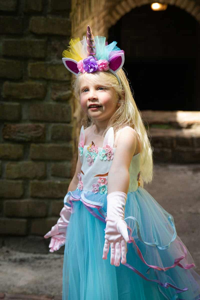 Meisje draagt de blauwe prinsessenjurk van Het Betere Merk met eenhoornhaarband, bloemenversiering en lange witte handschoenen.