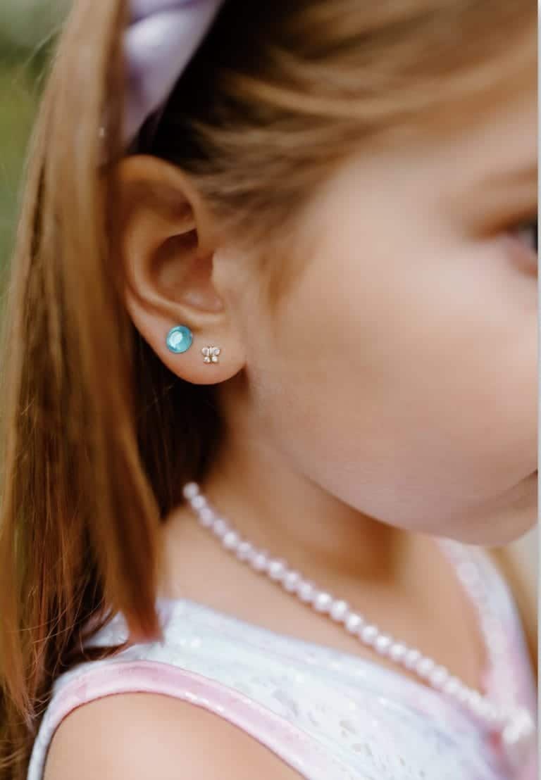 Close-up van een meisje met een blauw rond oorsticker en een wit bloemvormig oorstickertje op haar oor