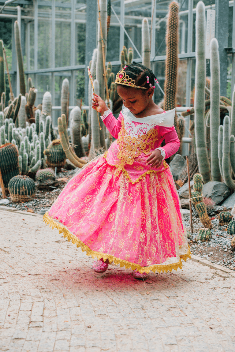 Meisje in een roze Doornroosje jurk kind met gouden versieringen, tiara en toverstaf tussen de cactussen