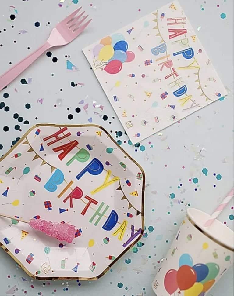 Happy Birthday-servetten met kleurrijke letters, ballonnen en feestelijke motieven op een tafel met confetti