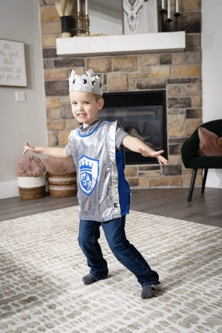 Jongen draagt een ridder outfit kind met glanzend zilveren vest, blauw schild en zilveren kroon.