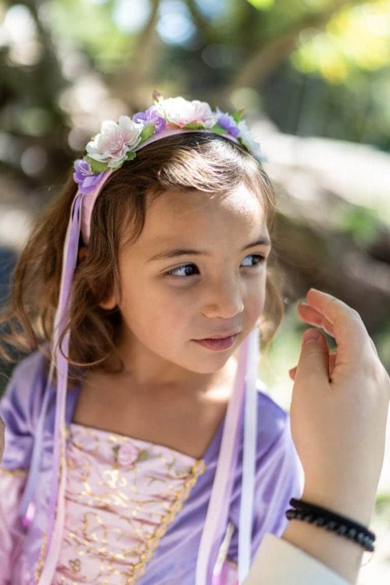 Meisje draagt een paars prinsessen diadeem met roze en witte bloemen en linten langs haar gezicht.