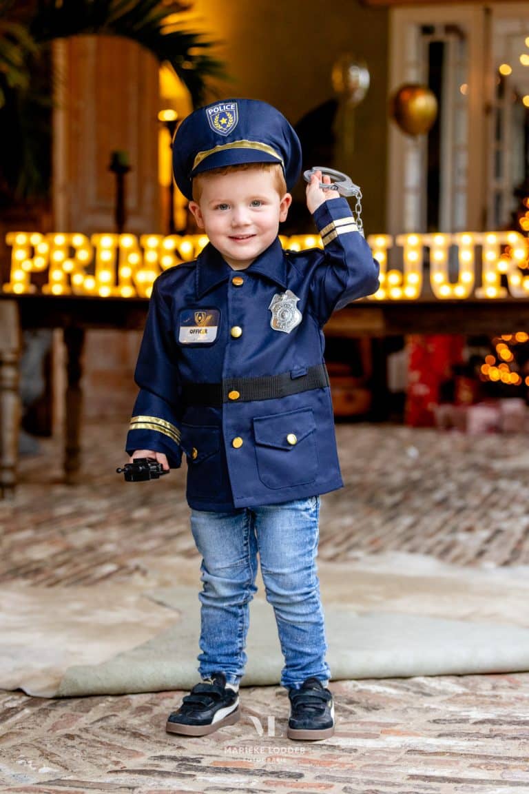 Jongen draagt een donkerblauwe verkleedset politie kind met politiehoed, jas en handboeien in de hand.