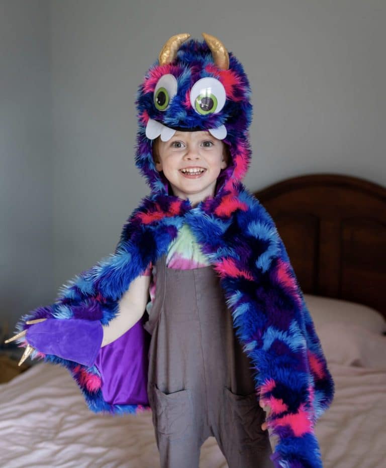 Kind draagt de blauw-fuchsia Goober monstercape met hoogpolige vacht, hoorns, grote ogen en tanden
