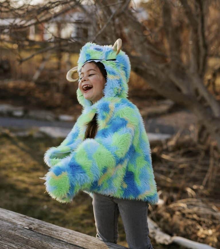 Kind draagt de blauwgroene Swampy Monstercape met zachte hoogpolige vacht, hoorns en monsteroog in het bos.