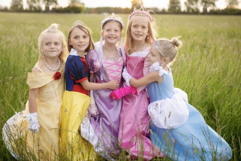 Meisje in een gele sneeuwitje jurk tussen vier kinderen in andere prinsessenjurken in een bloemenweide.