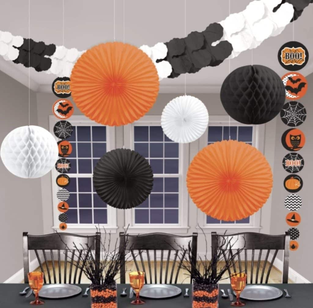 Halloween slingers in zwart, wit en oranje hangen boven een feestelijk gedekte tafel met papieren waaiers en decoraties