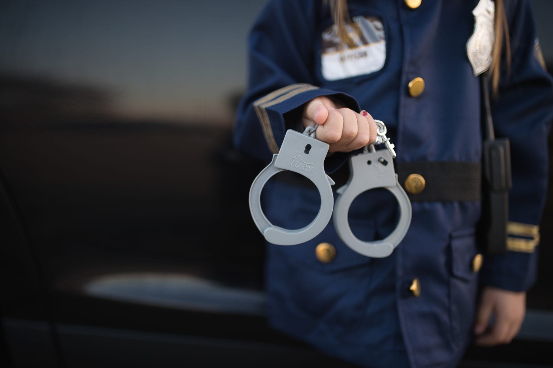 Handboeien van een donkerblauw politiepak voor kinderen, vastgehouden door een kind in politie-uniform.