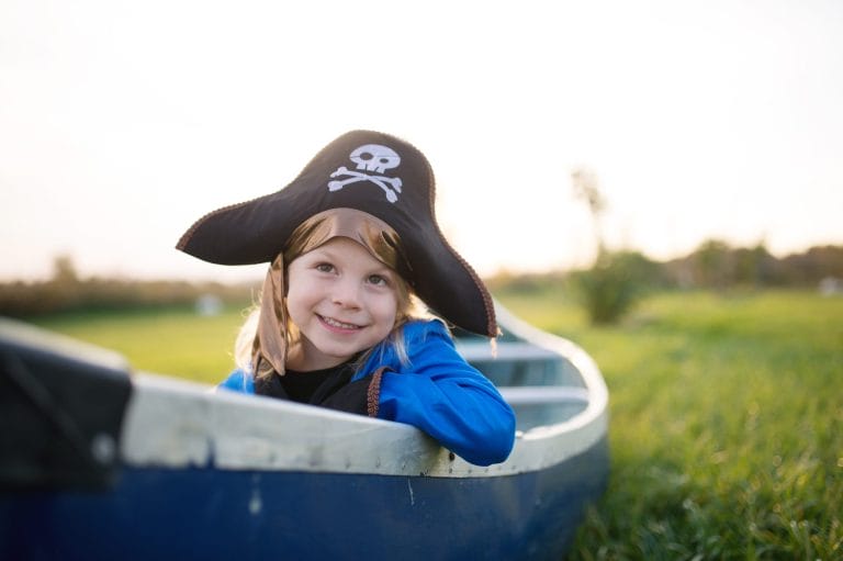 Lachend meisje in het blauwe Piratenkostuum, van dichtbij gezien in een boot buiten, met zwarte piratenhoed.