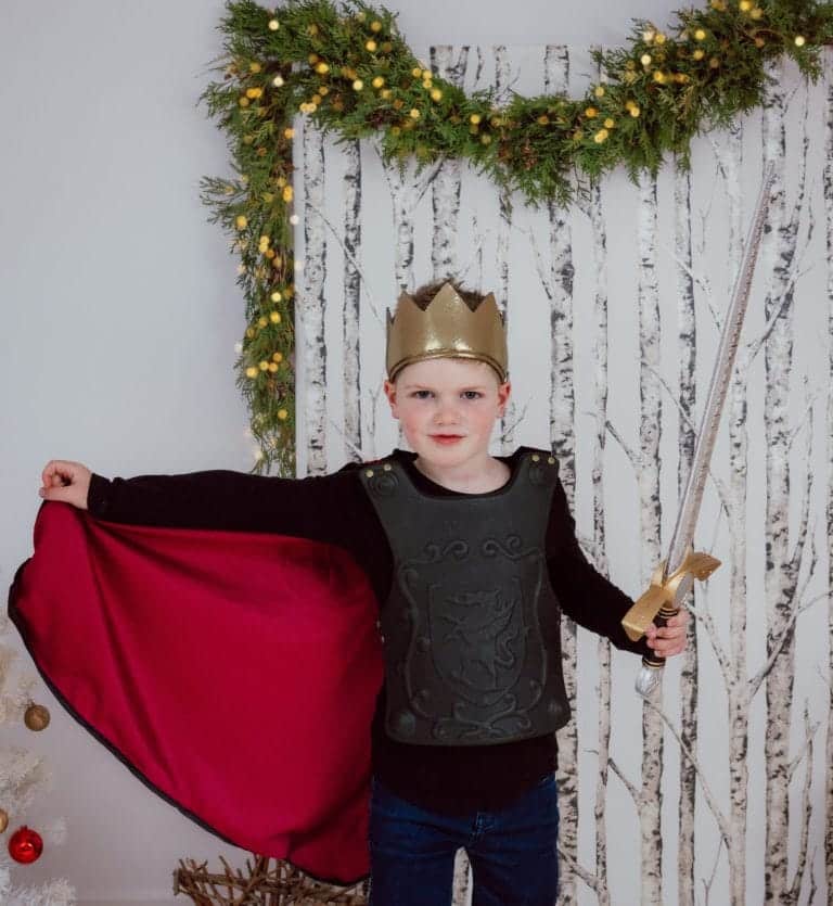 Jongen draagt Great Pretenders verkleedkleding als ridder, met rode cape, zwart harnas, gouden kroon en speelgoedzwaard.