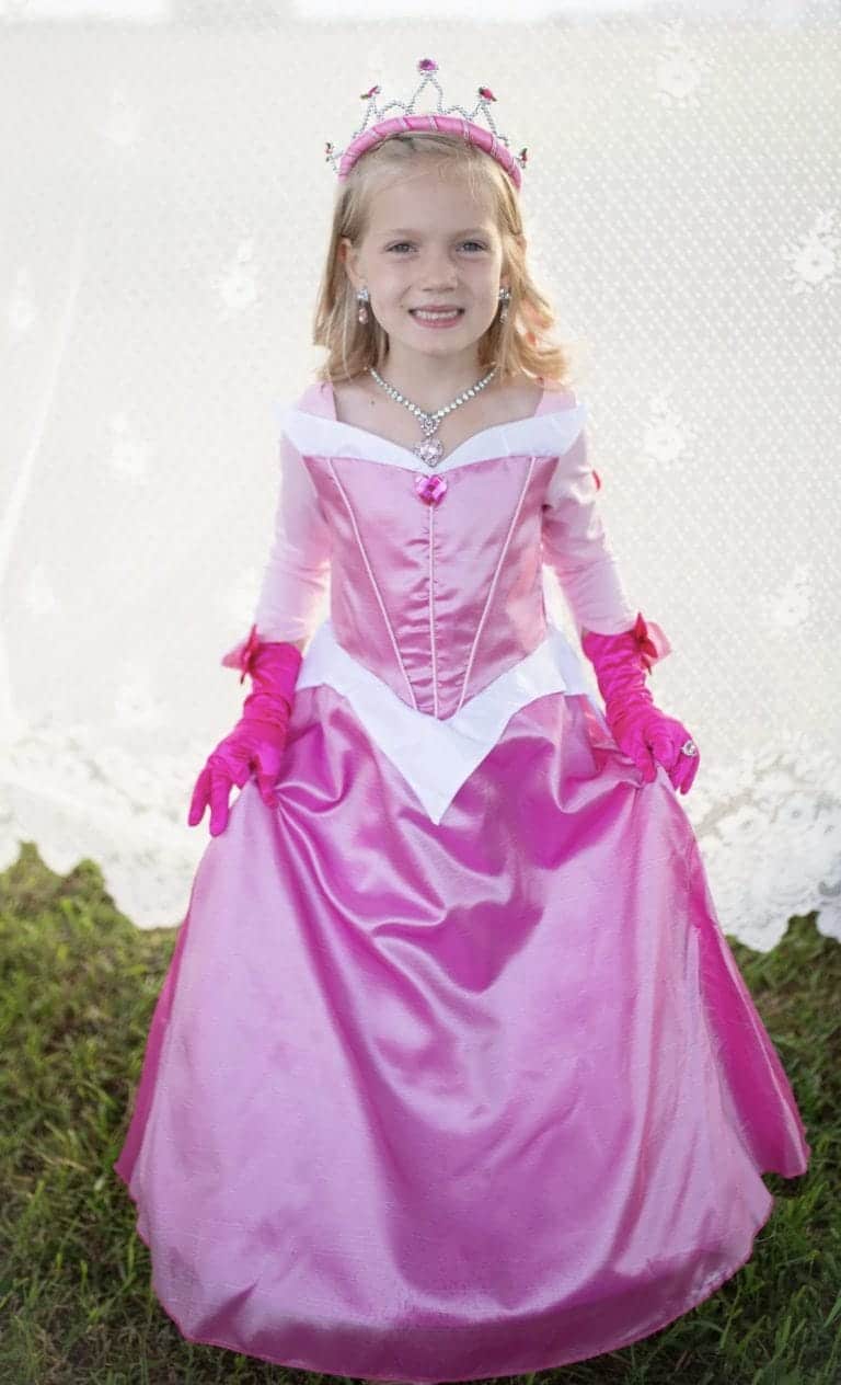 Roze Doornroosje prinsessenjurk in vooraanzicht, gedragen door een meisje buiten op gras met tiara en lange handschoenen