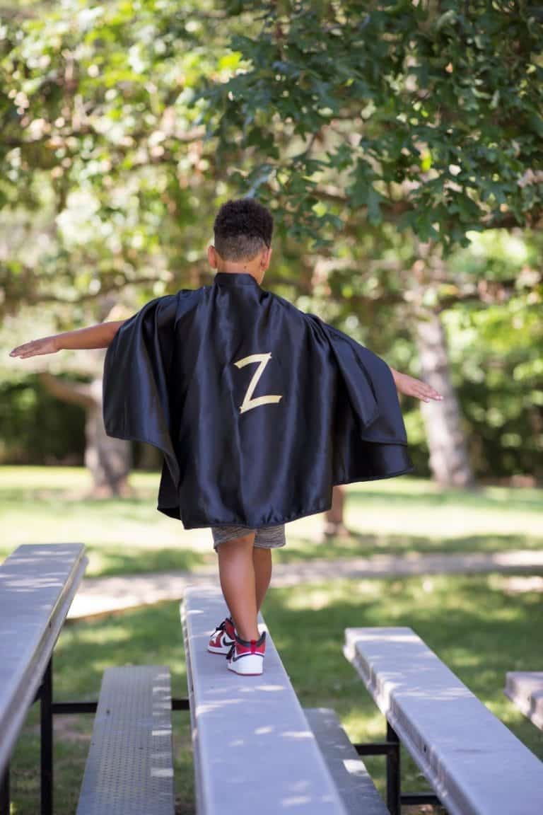 Jongen draagt als Zorro superheld een zwarte cape met groot goudkleurig Z-embleem op de rug