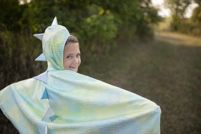 Kind draagt een lichtgroene drakencape met puntige capuchon en rugstekels buiten in het bos