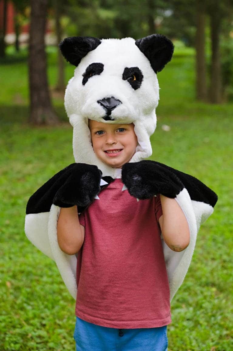 Jongen draagt een zwart-witte panda cape met grote pandakop en zwarte pootzakken in het bos