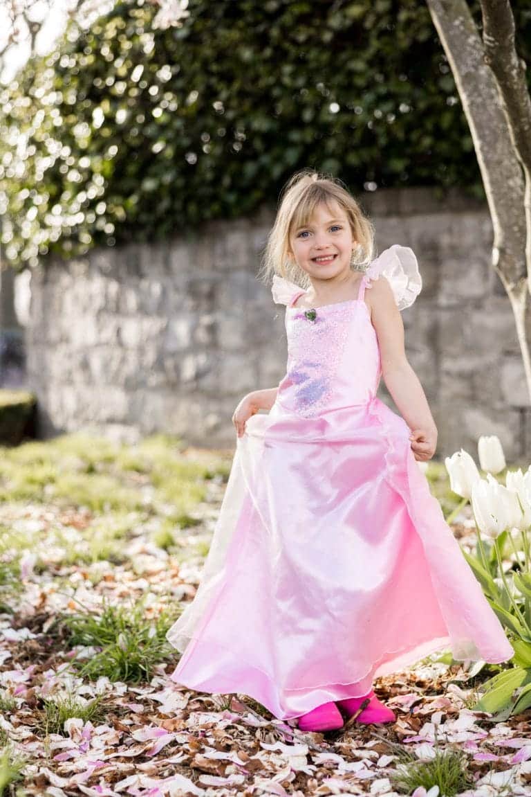 Meisje draagt een lichtroze Great Pretenders prinsessenjurk met glanzend lijfje en lange rok in een tuin