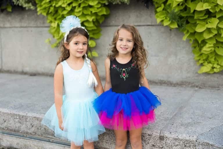 Twee meisjes dragen Great Pretenders Frozen jurken: een lichtblauwe Elsa-jurk en een zwarte Anna tutu-jurk met roze en blauwe tule