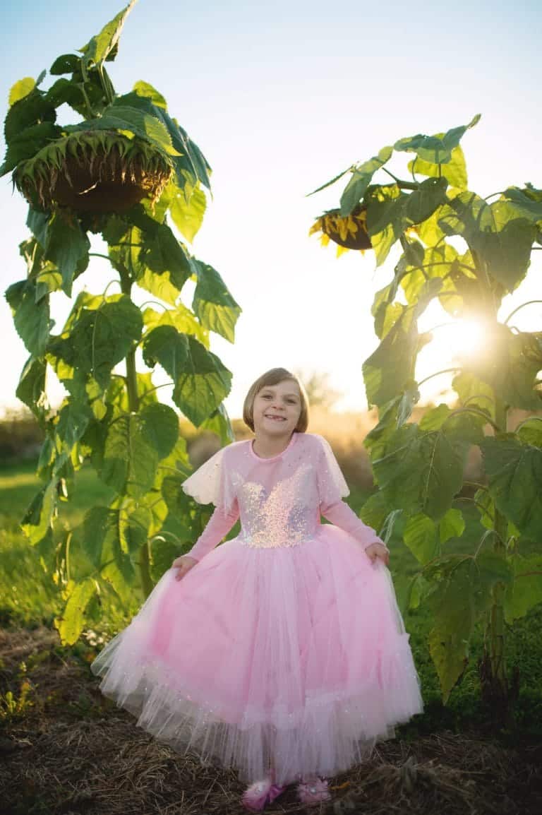 Meisje draagt een roze prinsessenjurk van Great Pretenders met glinsterend lijfje en volle tule rok tussen zonnebloemen.