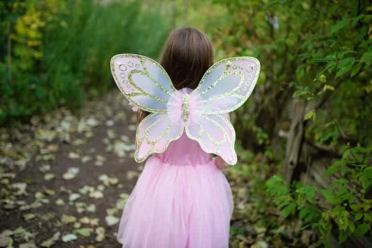 Meisje van achteren in de roze Great Pretenders vlinderjurk met glinsterende vleugels in een groen bos