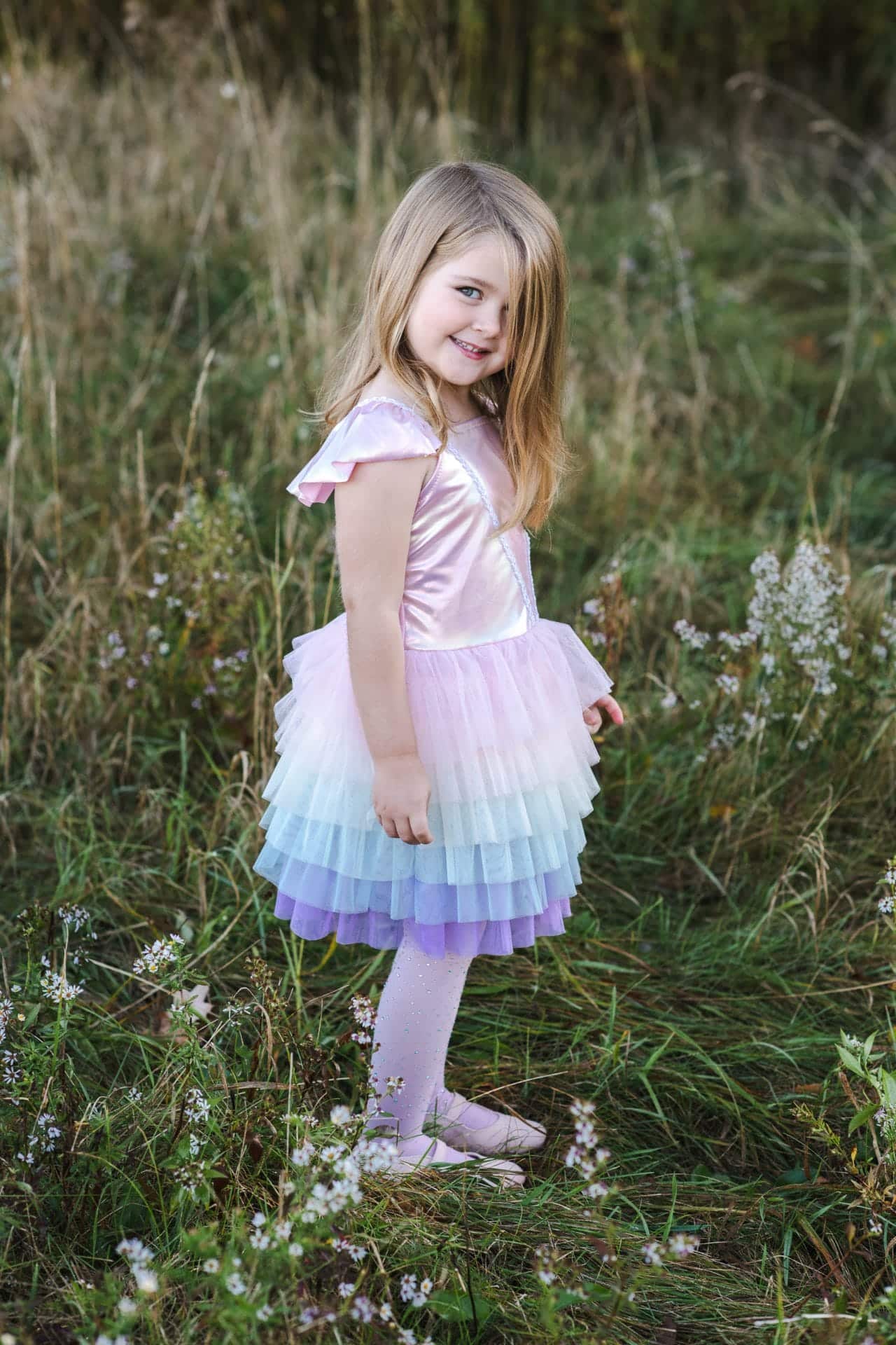 Meisje draagt de Great Pretenders regenboog tutu verkleedjurk met roze top en gelaagde tule rok in het gras