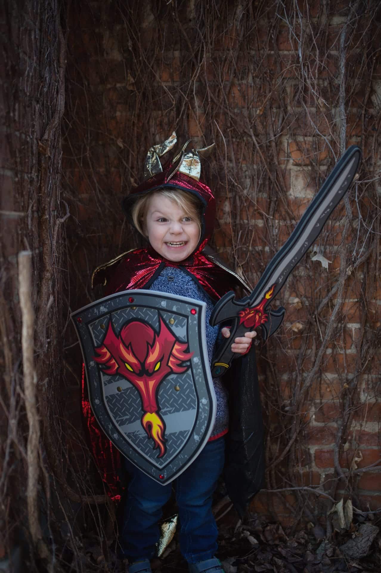 Kind met een ridder verkleedset houdt het drakenschild met een vuurspuwende draak vast