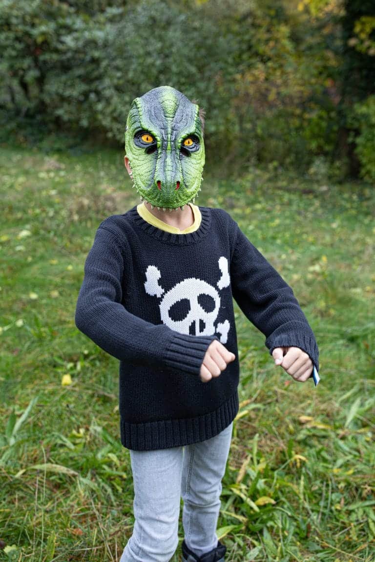 Kind draagt een groen Tyrannosaurus dinomasker met schubben en gele ogen in het bos