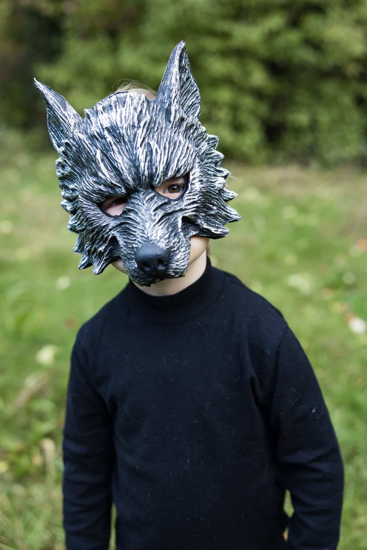 Kind draagt een grijs Great Pretenders masker weerwolf met puntige oren en een grote zwarte snuit in het groen
